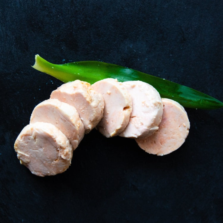 Sliced Monkfish liver on a dark surface garnished with a green leaf