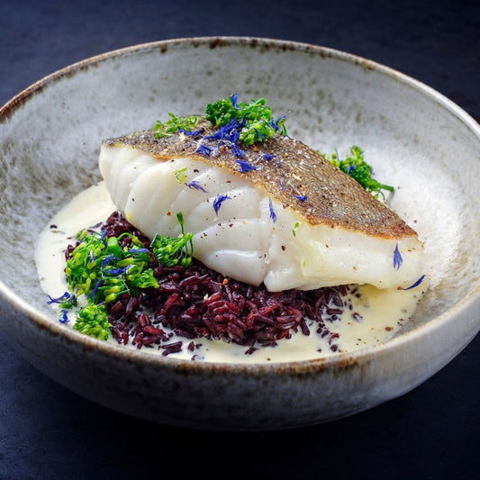 Pan-seared sablefish fillet served over a bed of black rice with a creamy sauce, garnished with fresh herbs