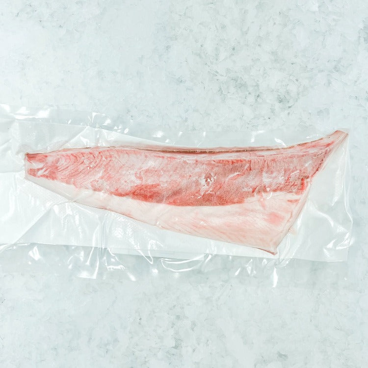Vacuum-sealed Hamachi loin belly part displayed on a white marble surface, showcasing the freshness and quality of the fish.