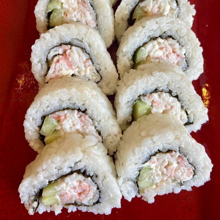 A platter of California rolls made with shredded imitation crab meat, cucumber, and avocado, wrapped in rice and seaweed. The sushi rolls are neatly arranged on a red plate, showcasing the creamy texture and pinkish-white color of the imitation crab filling