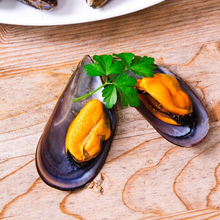 Cooked Mediterranean mussels half shell garnished with parsley on a wooden board
