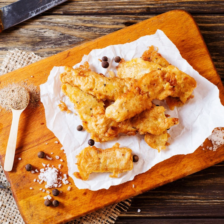 Crispy fried Pollock fillets on a wooden cutting board with spices