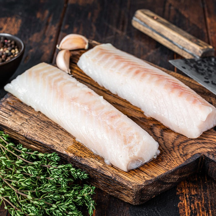 Raw Pollock fillets on a wooden board with garlic and herbs