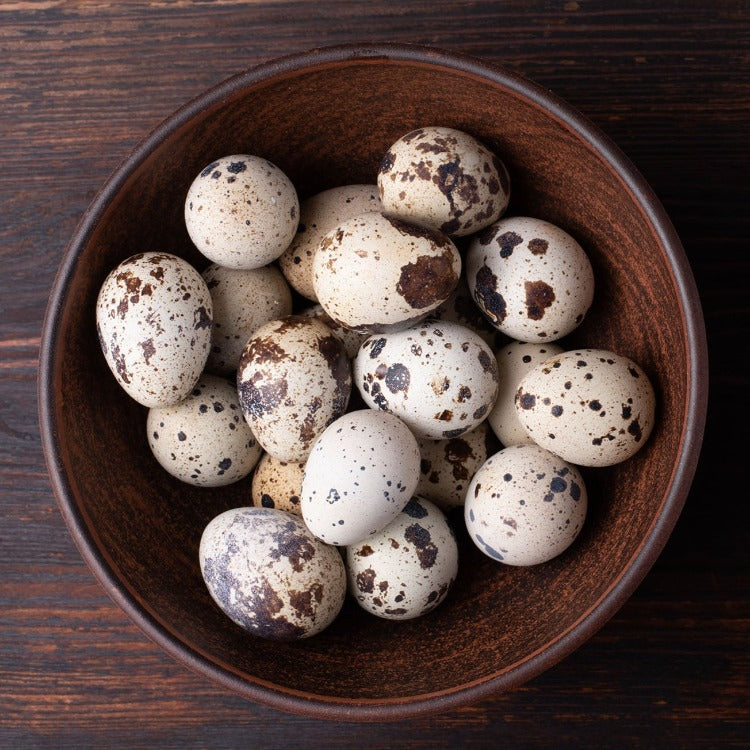 A glass bowl overflowing with spotted quail eggs, highlighting their unique appearance and freshness. Great for high-end cuisine and special occasions.