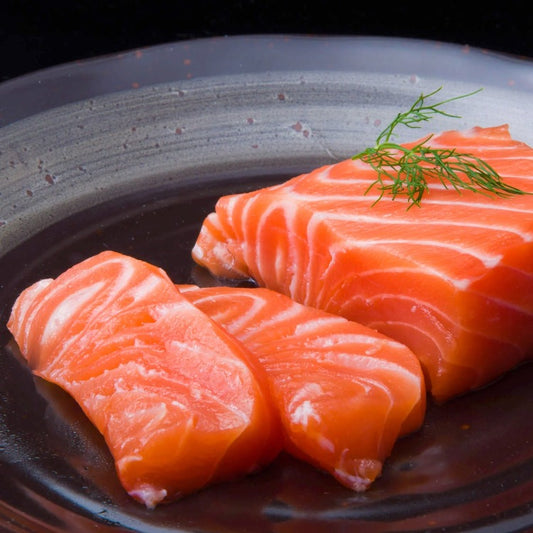 Fresh salmon fillet pieces on a dark plate, garnished with dill. Ideal for sashimi, sushi, or cooking, showcasing the high-quality, rich texture of Atlantic salmon