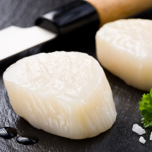 Fresh raw scallops placed next to a knife, ready for preparation
