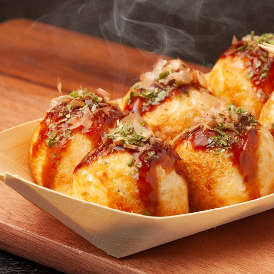 Freshly made Takoyaki grilled octopus balls garnished with bonito flakes and sauce, served on a wooden plate