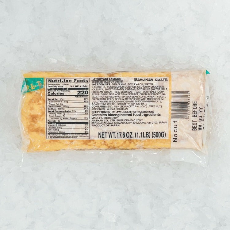 A tamagoyaki block in transparent plastic packaging, with nutritional facts visible on the label. The block is uniformly yellow, suggesting a smooth, spongy texture typical of tamagoyaki, and is placed on a bed of crushed ice to emphasize freshness