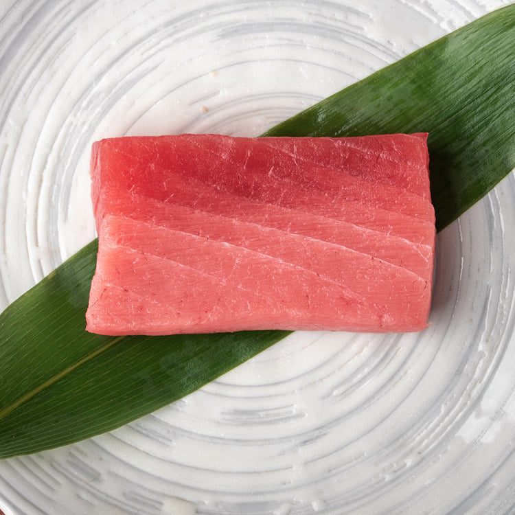 Fresh Bluefin Tuna loin cut placed on a green leaf on a white plate, showcasing the rich marbling and deep red color, perfect for sashimi or sushi.