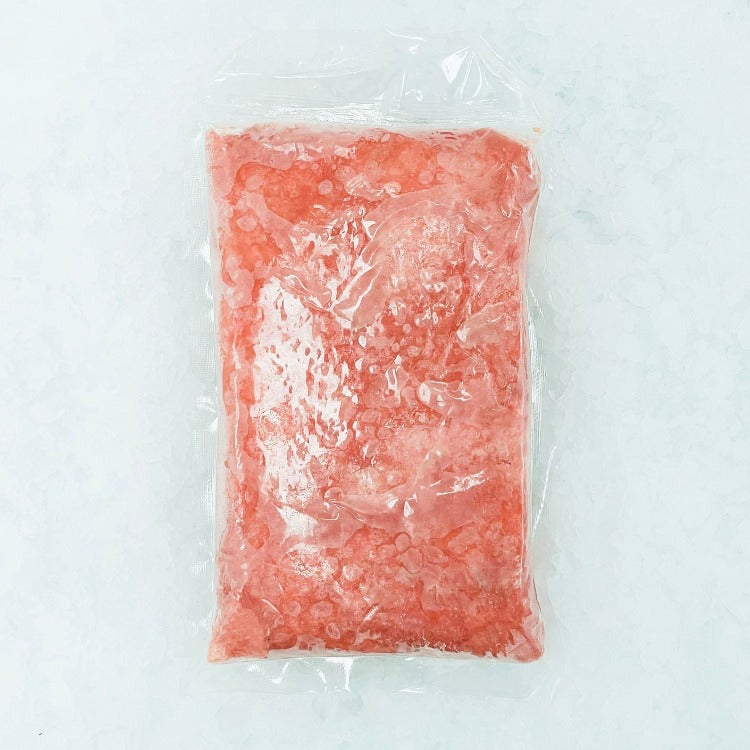 A frozen package of ground yellowfin tuna, shown in a clear plastic bag over a bed of crushed ice. The tuna appears finely ground, with a vibrant red-pink color, indicating its freshness and quality