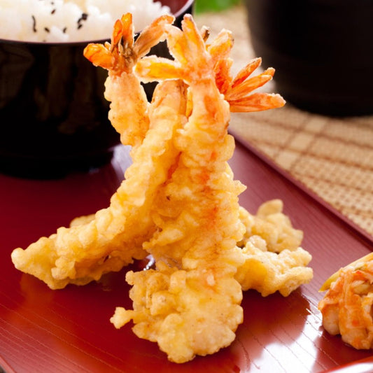 Close-up of crispy tempura shrimp served on a plate, with a bowl of rice in the background