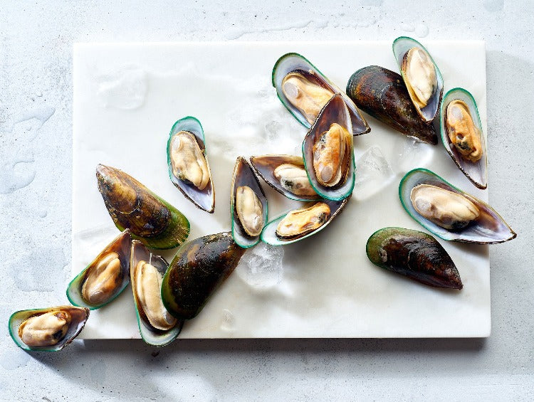 Fresh half-shell mussels elegantly arranged on a marble slab with ice, highlighting the vibrant green shells and plump orange mussels, perfect for gourmet seafood dishes