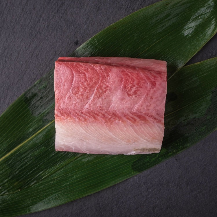 Fresh Hamachi loin belly part placed on green leaves, highlighting the rich marbling and premium quality of the fish.