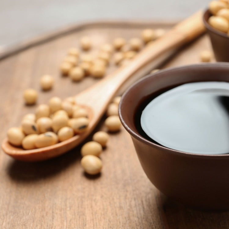 Close-up of soy sauce in a brown bowl with soybeans scattered on a wooden table. High-quality Yamasa Usukuchi Light Soy Sauce, ideal for traditional Japanese cuisine