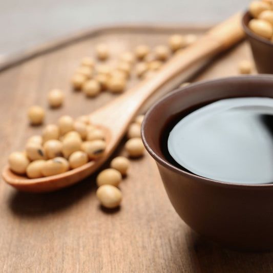 Close-up of soy sauce in a brown bowl with soybeans scattered on a wooden table. High-quality Yamasa Usukuchi Light Soy Sauce, ideal for traditional Japanese cuisine