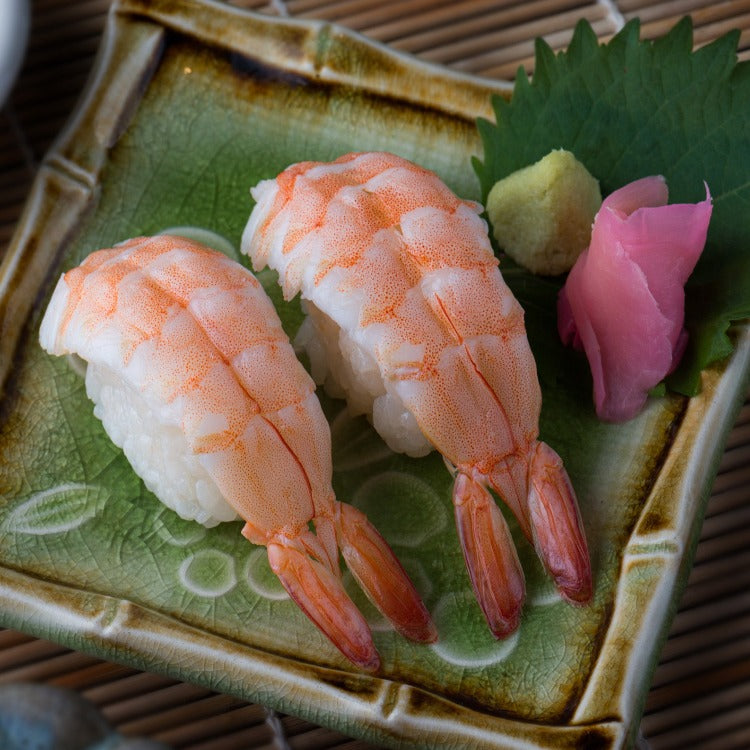 Three pieces of sushi ebi with pickled ginger and wasabi on a ceramic plate