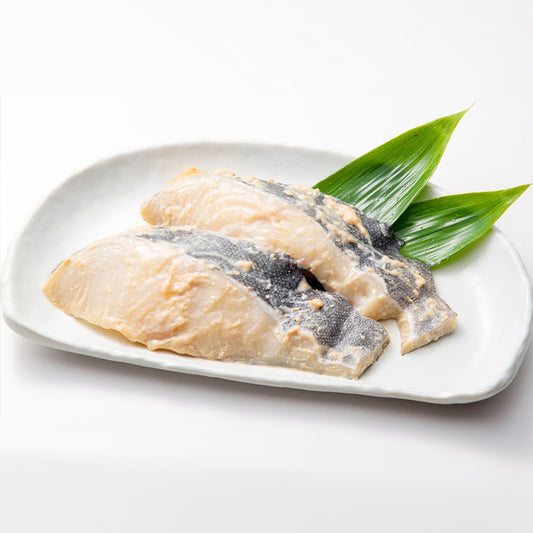 Raw Black Cod Kasuzuke marinated in sake lees, displayed on a white plate with fresh green leaves, ready for cooking