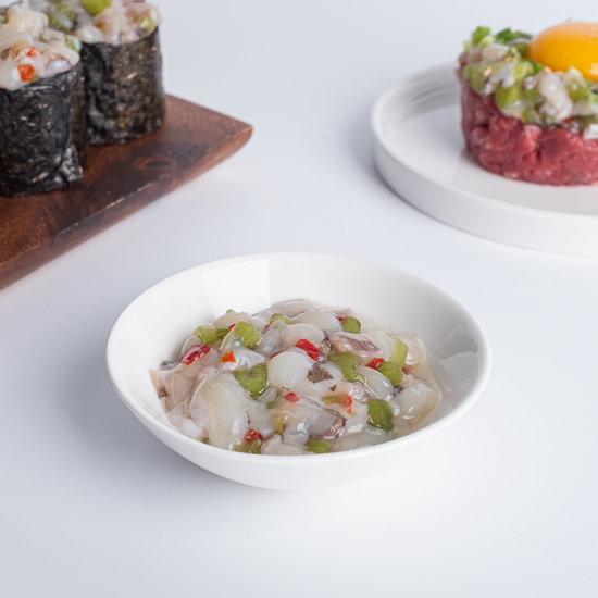 A bowl of seasoned chopped octopus mixed with vegetables, served as Tako Wasabi. The dish includes green peppers, red bell peppers, and sesame seeds, placed on a white background