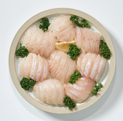 Freshly sliced Hirame sashimi (halibut fillet) garnished with parsley and lemon on a white platter