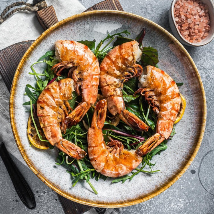 Salad with grilled white shrimp served on a plate with fresh greens and lemon slices